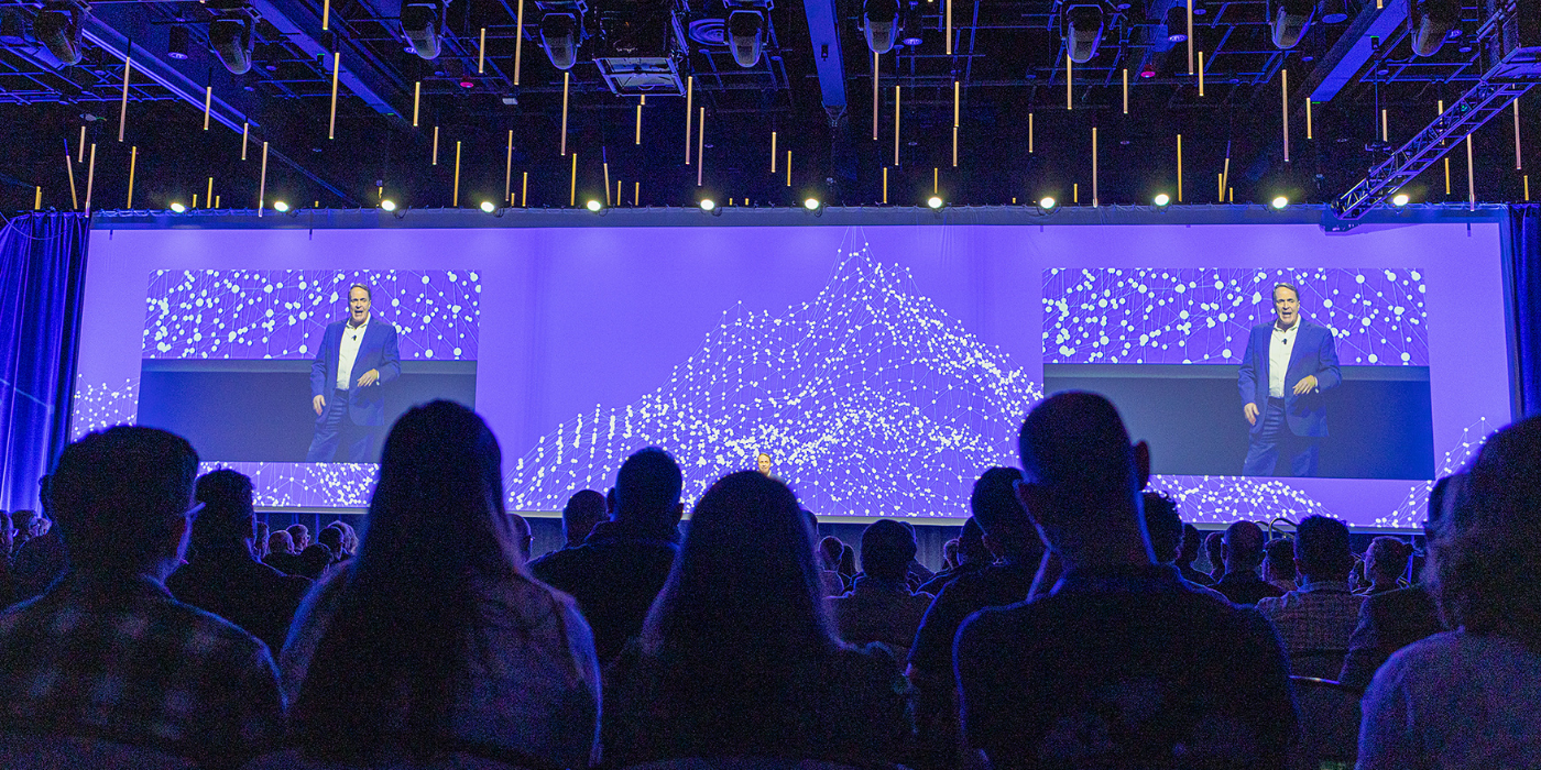 Keynote speaker on stage with large LED displays at corporate conference