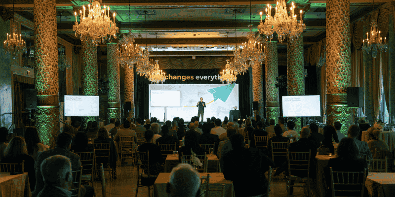 Presenter on stage in chandelier-lit ballroom