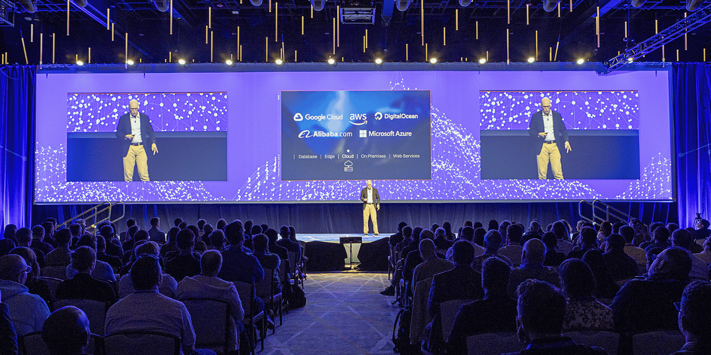 Speaker on purple-lit conference mainstage with LED wall
