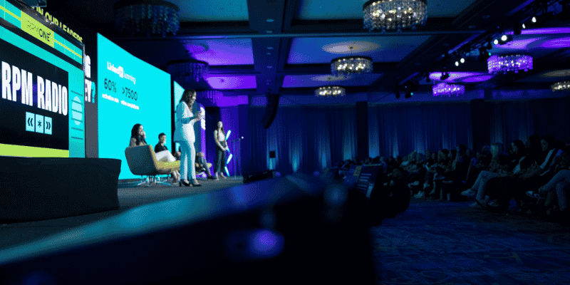 Presenter on stage with bold green and teal graphics